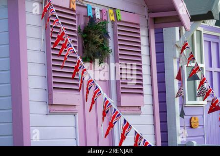 Union Jack Bunting sur une cabane colorée, pittoresque, rose et blanche de plage sur Westward Ho! Front de mer surplombant la plage et l'estuaire de Torridge. Banque D'Images