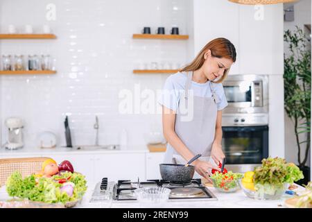 belle jeune femme essayant de cuisiner des aliments sains salade mélange de légumes à la cuisine à la maison Banque D'Images