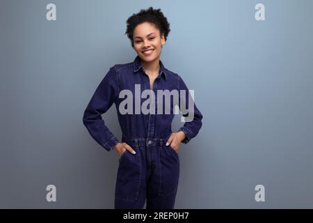 une jeune femme à la peau foncée et aux cheveux noirs est habillée d'un costume de genim bleu Banque D'Images