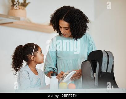 Mère emballant le déjeuner pour sa fille pour la santé, des collations de bien-être dans la cuisine de leur maison. Heureuse, solidaire et jeune maman parlant et se préparant Banque D'Images