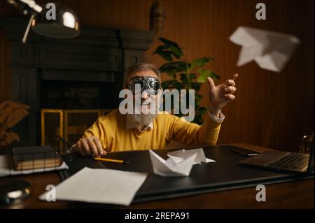 Drôle homme mature surjoyé portant des lunettes de pilote jouant avec l'avion origami Banque D'Images