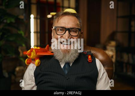 Portrait de riche homme d'affaires senior assis dans un fauteuil en cuir avec des jouets Banque D'Images