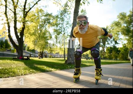 Homme senior portant des lunettes drôles monte sur des patins à roulettes dans le parc Banque D'Images
