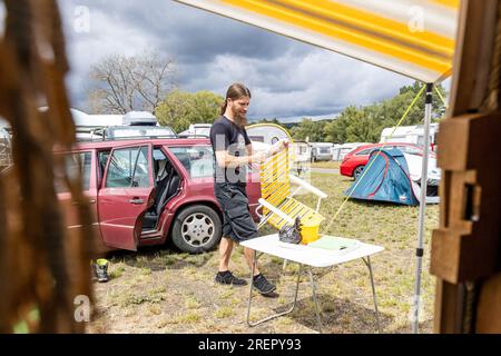 29 juillet 2023, Hesse, Wettenberg-Wißmar : Matthias Ibele installe son mobilier de camping au camping sur le lac de Wißmar. Avec son partenaire de vie, il est de Riedhausen près de Ravensburg pour visiter le festival Golden Oldies à Wettenberg. Malgré le mauvais temps, de nombreux campings en Hesse sont entièrement occupés. Photo : Christian Lademann/dpa Banque D'Images