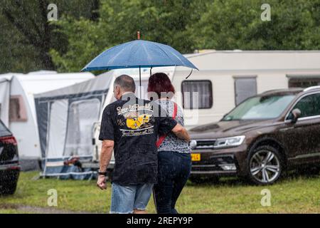 29 juillet 2023, Hesse, Wettenberg-Wißmar : les visiteurs du festival Golden Oldies marchent avec des parasols vers leurs caravanes au camping Wißmarer See. Malgré le mauvais temps, de nombreux campings en Hesse sont entièrement occupés. Photo : Christian Lademann/dpa Banque D'Images