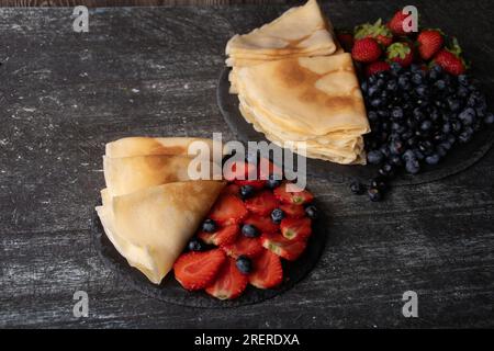 photo tranches de fraises et de bleuets sur une assiette avec des crêpes minces sur un fond sombre Banque D'Images