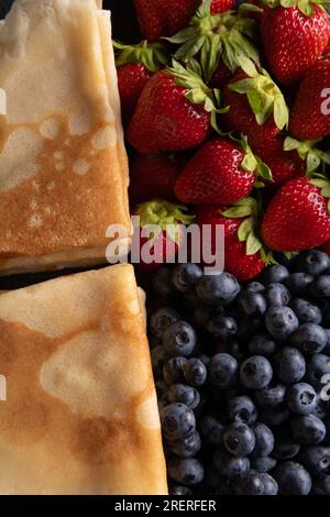 photo de crêpes fines fraîches frites avec fraises juteuses mûres et bleuets gros plan Banque D'Images