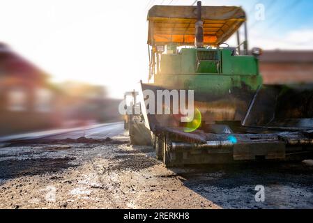 Machine de finisseur travaillant sur le chantier de construction de route au coucher du soleil, arrière-plan flou Banque D'Images