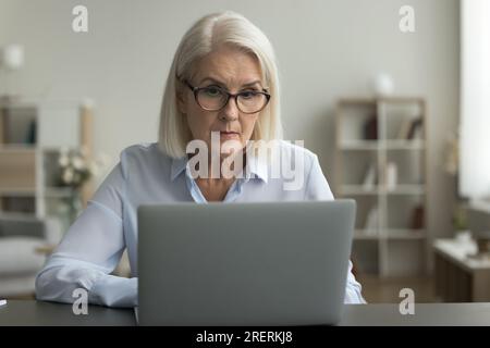Femme d'affaires mûre sérieuse dans les lunettes travaillant à l'ordinateur portable Banque D'Images