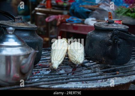 Les épis de maïs et les bouilloires à thé sont chauffés sur un barbecue au charbon de bois dans un marché du nord du Vietnam en hiver Banque D'Images