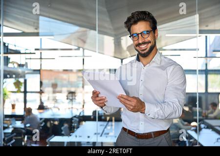 Heureux jeune homme d'affaires latin vérifiant les documents financiers dans le bureau. Banque D'Images