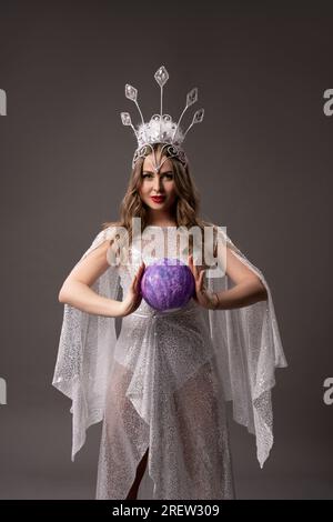 Douce fée en robe translucide blanche avec boule magique dans ses berges Banque D'Images