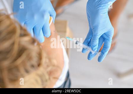 Grand angle de culture méconnaissable femelle médic dans des gants en latex injectant le vaccin coronavirus dans l'épaule du patient en clinique Banque D'Images