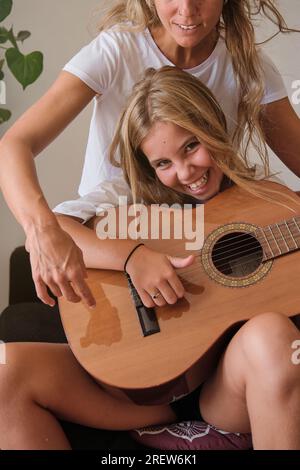 Excité positive jeune femme avec sourire toothy assis sur le canapé et jouant de la guitare acoustique en bois tout en regardant la caméra Banque D'Images
