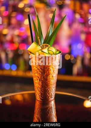 Cocktail mule alcoolisé de Moscou dans une tasse en cuivre décorée de concombre servi sur la table dans le bar sur fond flou avec bokeh Banque D'Images