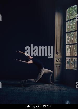 Vue latérale du gars se pliant en arrière et levant les bras contre la porte avec verre dans l'appartement sombre Banque D'Images