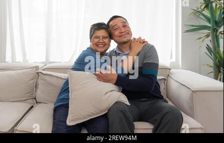 Un doux couple plus âgé profite du temps calme ensemble, assis confortablement sur leur canapé vintage dans un salon chaleureux et accueillant, rappelant des décennies de Banque D'Images