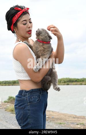 Jolie femelle asiatique lui tiennent les yeux oranges d'un chat Scottish Fold sur fond blanc. Banque D'Images