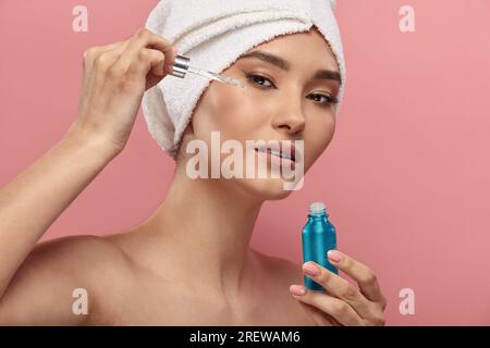 Fille asiatique en turban blanc de cheveux utilisant le sérum, rétinol. Banque D'Images