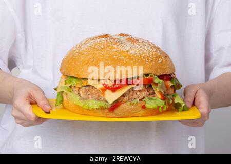 Les mains tiennent un plateau avec un gros hamburger. Banque D'Images