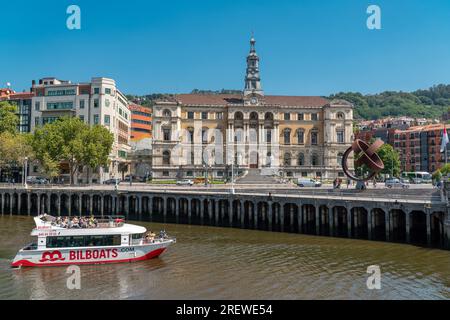 Magnifique bâtiment de l'Hôtel de ville de Bilbao. Devant le bâtiment se trouve la rivière Nervion. Bateau avec touriste au milieu de la rivière. Banque D'Images