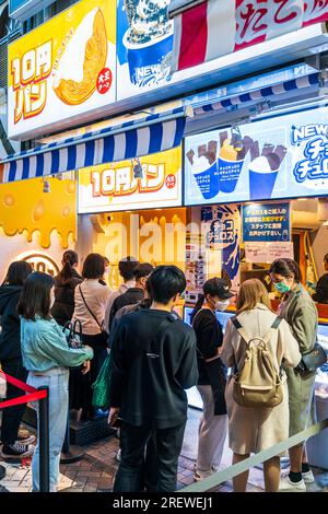 Masque portant des Japonais faisant la queue devant un comptoir de crème glacée dans la soirée à Dotonbori, le quartier de divertissement populaire d'Osaka, au Japon. Banque D'Images