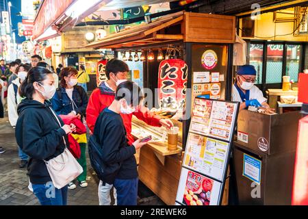 Des Japonais attendent le soir au comptoir à emporter du restaurant Takohachi servant des takoyaki et okonomiyaki, à Dotonbori, Osaka. Banque D'Images