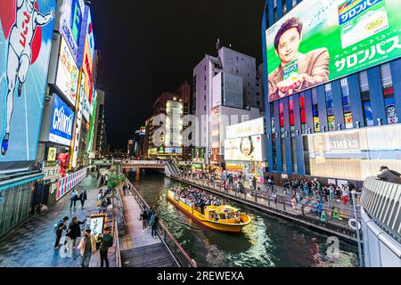 Vue depuis le pont d'Ebisu la nuit d'un bateau de croisière rempli de touristes sur la rivière avec le célèbre écran au néon Glico Running Man à Dotonbori, Osaka. Banque D'Images