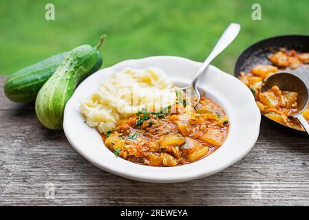 Manger un plat traditionnel slovène avec une sauce au concombre en purée de pommes de terre rouges. Concombres fraîchement cueillis du jardin. Nourriture d'été Banque D'Images