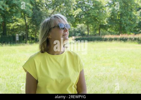 Portrait d'été d'une femme blonde avec en toile de fond une pelouse herbeuse et des arbres dans le parc Banque D'Images