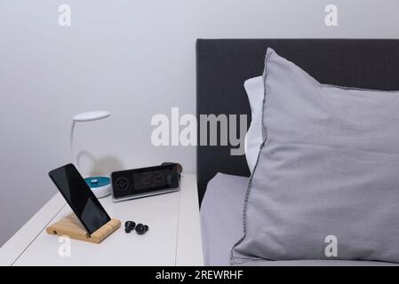 Chambre réelle. smartphone et casque sur la table de chevet avec lampe et horloge Banque D'Images