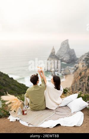 Vue arrière du couple buvant du champagne et des verres à clinking, profitant de la côte de l'océan, espace de copie, plan vertical Banque D'Images