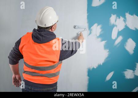 Le peintre applique la première couche de peinture claire sur un mur de couleur foncée Banque D'Images