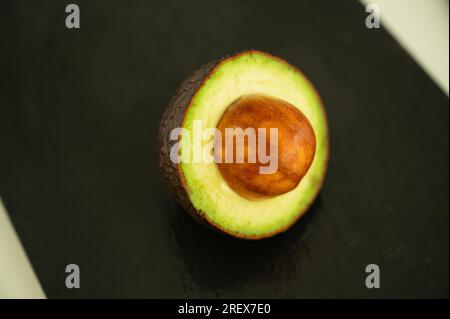 Demi avocat avec des graines dépassant sur fond noir - Superfood sain Banque D'Images