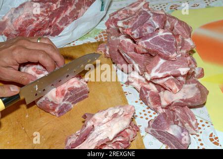 Mains de l'homme qui tranche un gros morceau de viande crue en petits morceaux par couteau tranchant. Banque D'Images