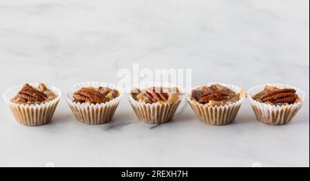 Tartelettes de noix de pécan au caramel sucré et salé toutes en ligne sur un fond clair. Banque D'Images