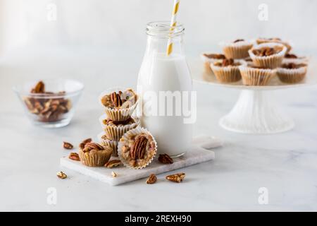 Un arrangement de tartelettes de noix de pécan au caramel salé avec une bouteille de lait de coco. Banque D'Images