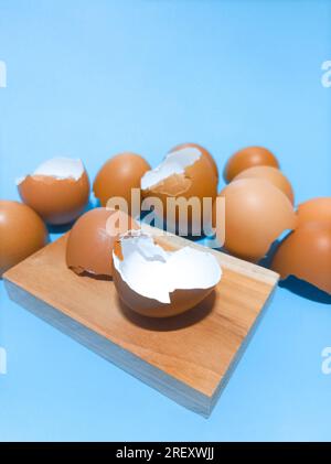 Coquilles d'œufs disposées sur une planche à découper sur un fond bleu. Banque D'Images