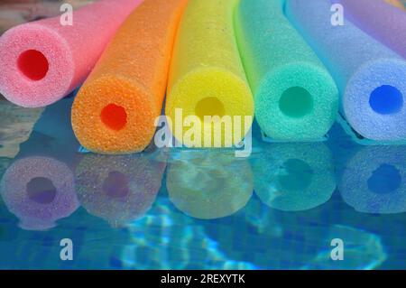 Nouilles de piscine en polyéthylène couleur arc-en-ciel flottant dans une piscine carrelée bleue, vibrations estivales Banque D'Images