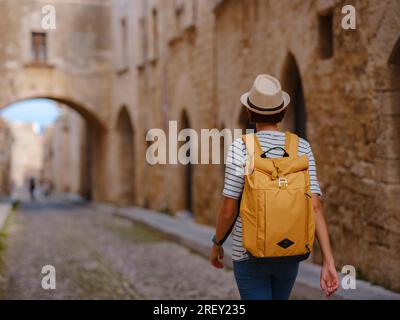 Voyage d'été à Rhodes île Grèce. Jeune femme asiatique en tshirt rayé et chapeau promenades rue des Chevaliers de fortifications château. voyageur féminin vis Banque D'Images