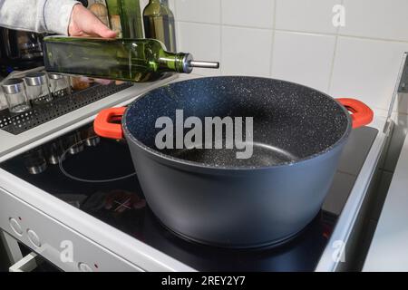 Main de femme avec une bouteille d'huile. Verser de l'huile dans une grande casserole sur la cuisinière pour la cuisson. Gros plan. Banque D'Images