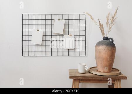 Tableau d'affichage en treillis métallique noir, tableau d'affichage avec maquettes de cartes mémoire vierges. Concept élégant d'intérieur de bureau à domicile. Vase en argile avec herbe sèche et tasse de Banque D'Images