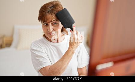 Femme d'âge moyen peignant les cheveux regardant sur le miroir à la chambre Banque D'Images