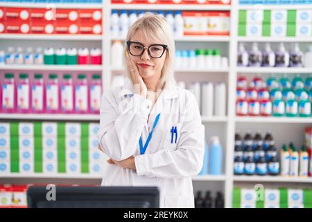 Jeune femme caucasienne travaillant à la pharmacie en pharmacie pensant à la fatigue et s'ennuyer avec des problèmes de dépression avec les bras croisés. Banque D'Images