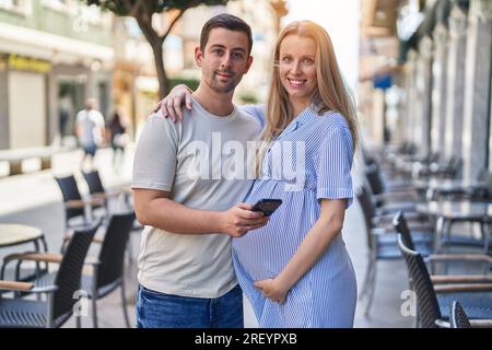 Homme et femme couple attendant bébé en utilisant smartphone à la terrasse du café Banque D'Images