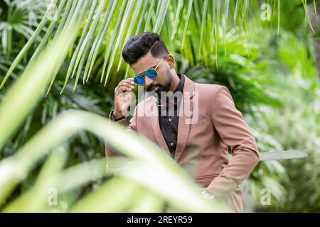 Beau jeune homme indien en costume et lunettes de soleil posant en plein air Banque D'Images