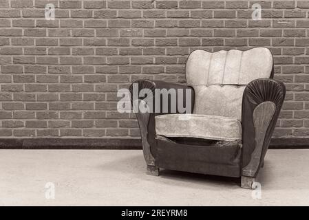 Fauteuil sans personne. Un vieux fauteuil avec des traces du temps contre un mur de briques. noir et blanc Banque D'Images