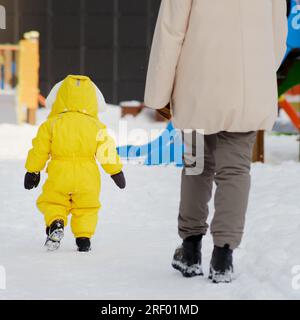 Bébé court dans la neige pour jouer sur l'aire de jeux d'hiver. Un enfant joyeux, un bonhomme de neige jaune, va à la maternelle. Enfant d'un an huit m Banque D'Images