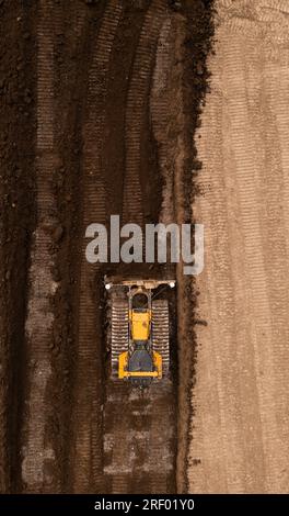 Vue aérienne directement au-dessus d'un bulldozer ou d'une machine de terrassement avec des chenilles poussant la terre et le sol dans l'industrie de la construction sur un site de friches industrielles wi Banque D'Images