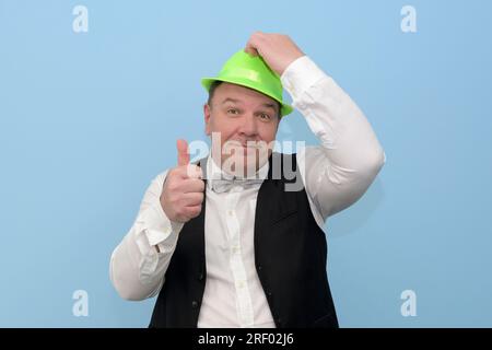 Bonne fête. Un homme d'âge moyen dans un chapeau vert de carnaval vous invite à une fête. fond bleu clair. Banque D'Images